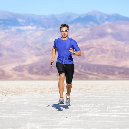 Running man - sprinting athlete runner in desert. Fit athletic male fitness model in fast sprint run at great speed towards camera. Sport in amazing extreme desert landscape.